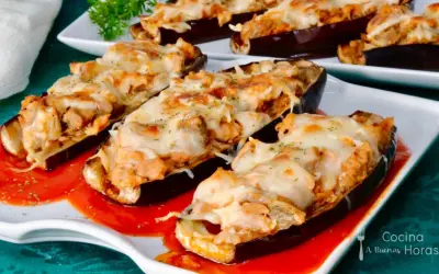 Berenjenas rellenas de atún gratinadas con queso, servidas sobre una base de salsa roja.