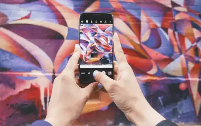 Zdjecie na Instagrama: ręce trzymają telefon, robiąc zdjęcie kolorowego muralu.