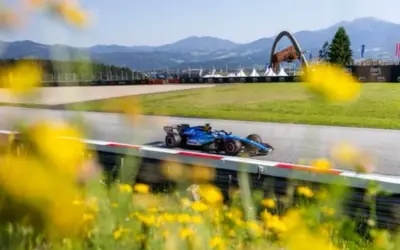 Un coche de F1 azul compite en un circuito soleado, con flores amarillas en primer plano. ¡Un gran resultado f1 hoy!