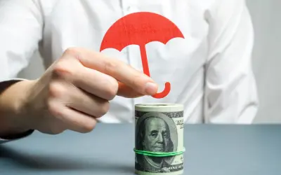 Dłoń trzyma czerwony parasol nad zrolowanymi dolarami. Tani murek oporowy dla Twoich finansów.