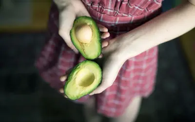 Hände halten eine aufgeschnittene Avocado, bereit für eine pflegende Avocado-Maske für die Haare.