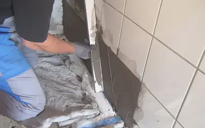 Hand trägt Abdichtung auf alten Fliesen auf.