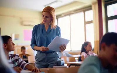 Nauczycielka z dokumentami w ręku, skupiona na uczniu. Jej zaangażowanie to klucz do awansu zawodowego nauczyciela.