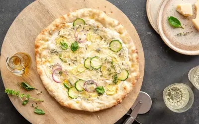 Pyszna pizza bianca z cukinią, cebulą i cytryną, podana na drewnianej desce.