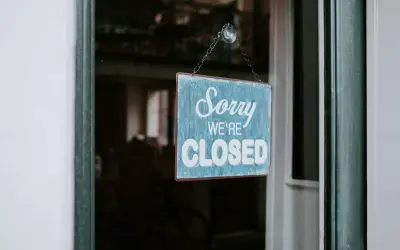 En blå skylt med texten "Sorry WE'RE CLOSED" hänger i ett fönster. Enskild firma i vilande.