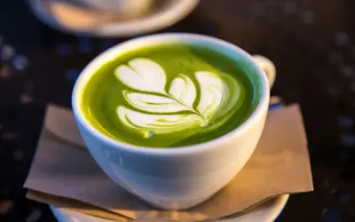 En vit kopp med grön matcha latte, dekorerad med ett vitt mönster som liknar ett löv. Matcha innehåll i sin finaste form.