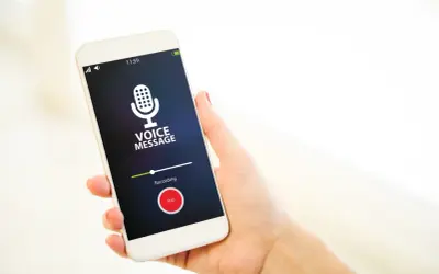 Dłoń trzyma smartfon z włączonym dyktafonem w telefonie. Na ekranie widnieje komunikat "VOICE MESSAGE" i przycisk "Stop".