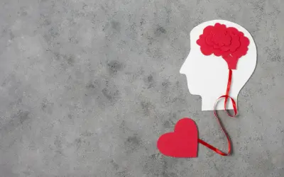 Czerwone serce połączone wstążką z mózgiem w profilu głowy. Symbolizuje to emocjonalne reakcje neurotyka.