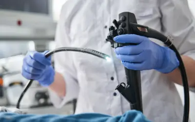 Lekarz w niebieskich rękawiczkach trzyma endoskop. W Warszawie NFZ oferuje kolonoskopię i gastroskopię w znieczuleniu ogólnym.