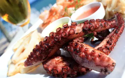 Tentáculos de pulpo a la plancha, dorados y jugosos, servidos con patatas y salsas.
