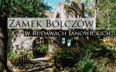 Kamienne ruiny zamku Bolczów w Rudawach Janowickich, porośnięte zielenią, z łukowym wejściem i drewnianym mostkiem.