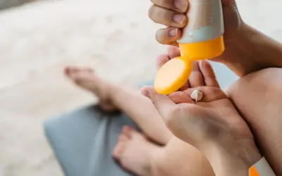 Manos aplicando crema solar caduca en la palma. Un niño descansa en una tumbona al fondo.