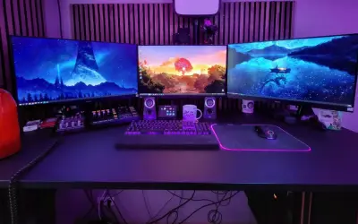 Ein episches **gaming set up** mit drei Monitoren, beleuchteter Tastatur und Maus. Im Hintergrund leuchtet lila Beleuchtung.