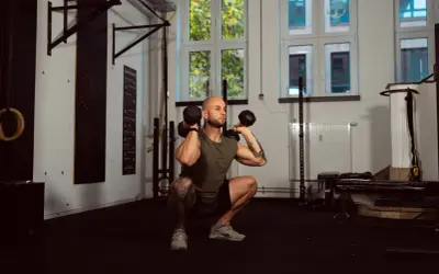 Mann macht Kniebeugen mit Kurzhanteln. Ein Supersatz ist, wenn zwei Übungen direkt hintereinander ohne Pause ausgeführt werden.