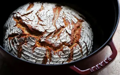 Frisch gebackenes Dinkel Mischbrot mit knuspriger Kruste und weißer Mehlschicht in einem roten Gusseisentopf.
