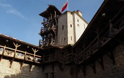 Zamek w Korzkwi z drewnianymi gankami i wieżą, na której powiewa polska flaga.