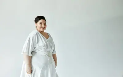 Uśmiechnięta panna młoda w pięknej, białej sukience weselnej plus size z ozdobnym pasem.