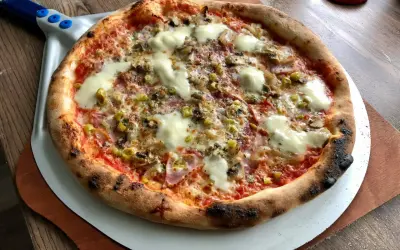 Upieczona pizza z serem, pieczarkami i oliwkami na łopacie do pizzy.