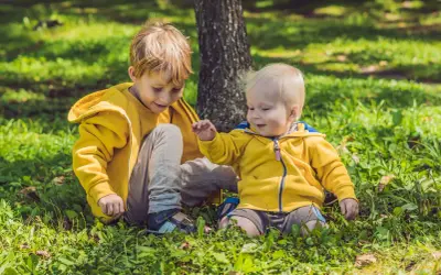 Dwóch chłopców w żółtych bluzach siedzi na trawie w parku.