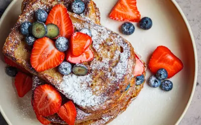 En hög med gyllene french toast, toppad med färska jordgubbar, blåbär och pudersocker. Ett perfekt recept för en lyxig frukost.