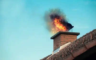 Płomienie i dym wydobywają się z ceglanego komina w domu, tworząc dramatyczny widok na tle błękitnego nieba.