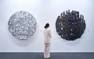 En kvinna i ljus kostym betraktar två runda konstverk med arabisk kalligrafi. Det vänstra är i metall, det högra i mörkare material. En atra daniel.