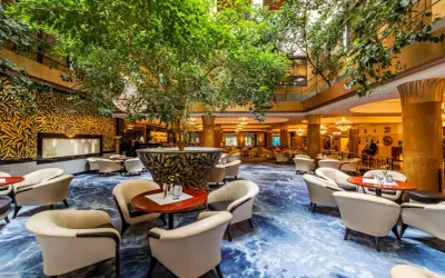 Luksusowy hol hotelowy z bujną roślinnością, wygodnymi fotelami i ozdobnym dywanem. Idealne miejsce na relaks w sieci luksusowych hoteli.