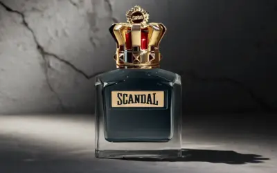 Elegancka butelka perfum Scandal męskie z koroną na nakrętce, stojąca na tle pękniętej ściany.