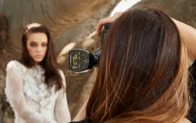 Fotografka z zimną stopką na aparacie celuje w modelkę w białej sukni.