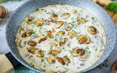 Cremige Rahmsauce mit frischen Champignons, verfeinert mit Petersilie, in einer Pfanne.
