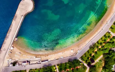 Vista aerea di una spiaggia e di un molo a Istanbul, dove c'è il mare turchese e una strada costiera con un parco verde.