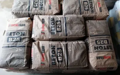 Sztaple worków z betonem B25. Na opakowaniach widnieje informacja o wadze 25kg, co pomaga oszacować, ile cementu na kubik betonu potrzeba do budowy.