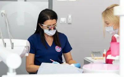 Dentystka w okularach powiększających i masce pracuje nad pacjentem, który odczuwa drętwienie po znieczuleniu zęba.