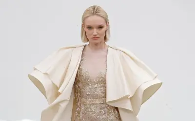 Modelka w kremowym, falbaniastym płaszczu i zdobionej sukni prezentuje dzieło haute couture.