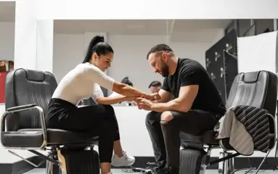 Barber w czarnym t-shircie i podartych jeansach siedzi na fotelu, trzymając dłoń klientki. Zastanawia się, ile zarabia barber.