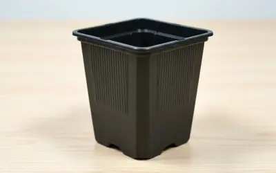 En svart, fyrkantig kruka med räfflade sidor står på ett ljust träbord. Perfekt för dina små plantor.
