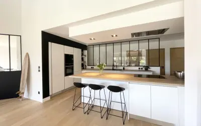 Cuisine moderne avec îlot central, plan de travail en bois et verrière industrielle. Une belle idée cuisine avec verriere pour un espace lumineux.