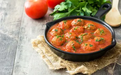 Pyszne pulpeciki w aromatycznym sosie pomidorowym, posypane natką pietruszki. Idealny sos do pulpetów na drewnianym stole.