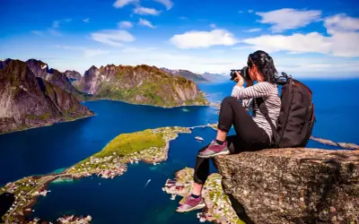 En fotograf fångar de dramatiska vyerna över Lofoten sevärdheter, med branta berg och en idyllisk by vid det blå havet.