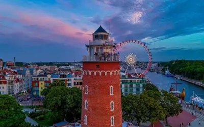 Widok na latarnię morską, diabelski młyn i port w Kołobrzegu o zachodzie słońca.