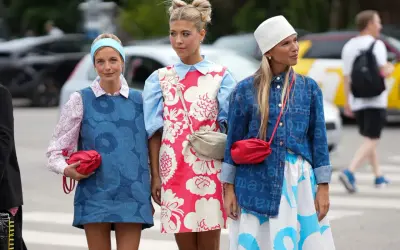 Trzy dziewczyny prezentują modny styl ubioru młodzieży: sukienki w kwiaty, dżinsowe kamizelki i kolorowe torebki.
