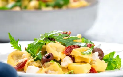 Ein köstlicher italienischer Salat mit Tortellini, Rucola, Oliven und getrockneten Tomaten auf einem Teller.