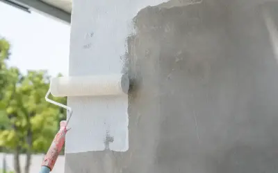 Malowanie betonu wałkiem. Biała farba pokrywa szarą ścianę, odświeżając jej wygląd.