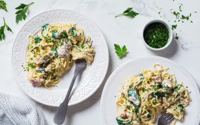 Dwa talerze spaghetti z kremowym sosem, szpinakiem i kawałkami tuńczyka z puszki, posypane natką pietruszki.