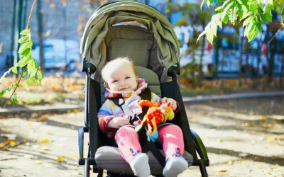 Uśmiechnięte dziecko w kolorowym sweterku i różowych skarpetkach siedzi w spacerówce, trzymając zabawkę. Od kiedy spacerówka stała się jego ulubionym miejscem na świecie.