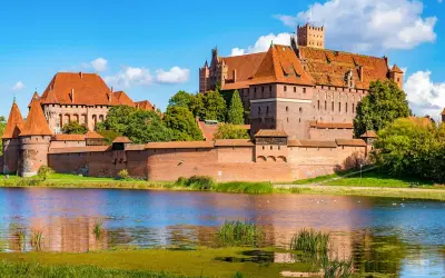 Die imposante Marienburg Burg, eine mittelalterliche Festung aus rotem Backstein, thront über einem ruhigen See.