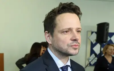 Rafał Trzaskowski, którego wykształcenie budzi zainteresowanie, w garniturze i krawacie. W tle inne osoby i tablica.