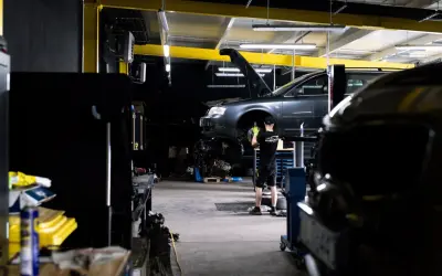 Mechanik bada przyczynę, dlaczego auto nie odpala. Podniesiony przód pojazdu i widoczny silnik sugerują skomplikowaną usterkę.