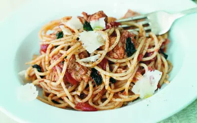 En portion tonfisksallad med pasta, toppad med parmesan och örter. En gaffel vilar i tallriken.
