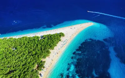 Zloty piasek i turkusowa woda na chorwackich plażach. W oddali widać łódź motorową.